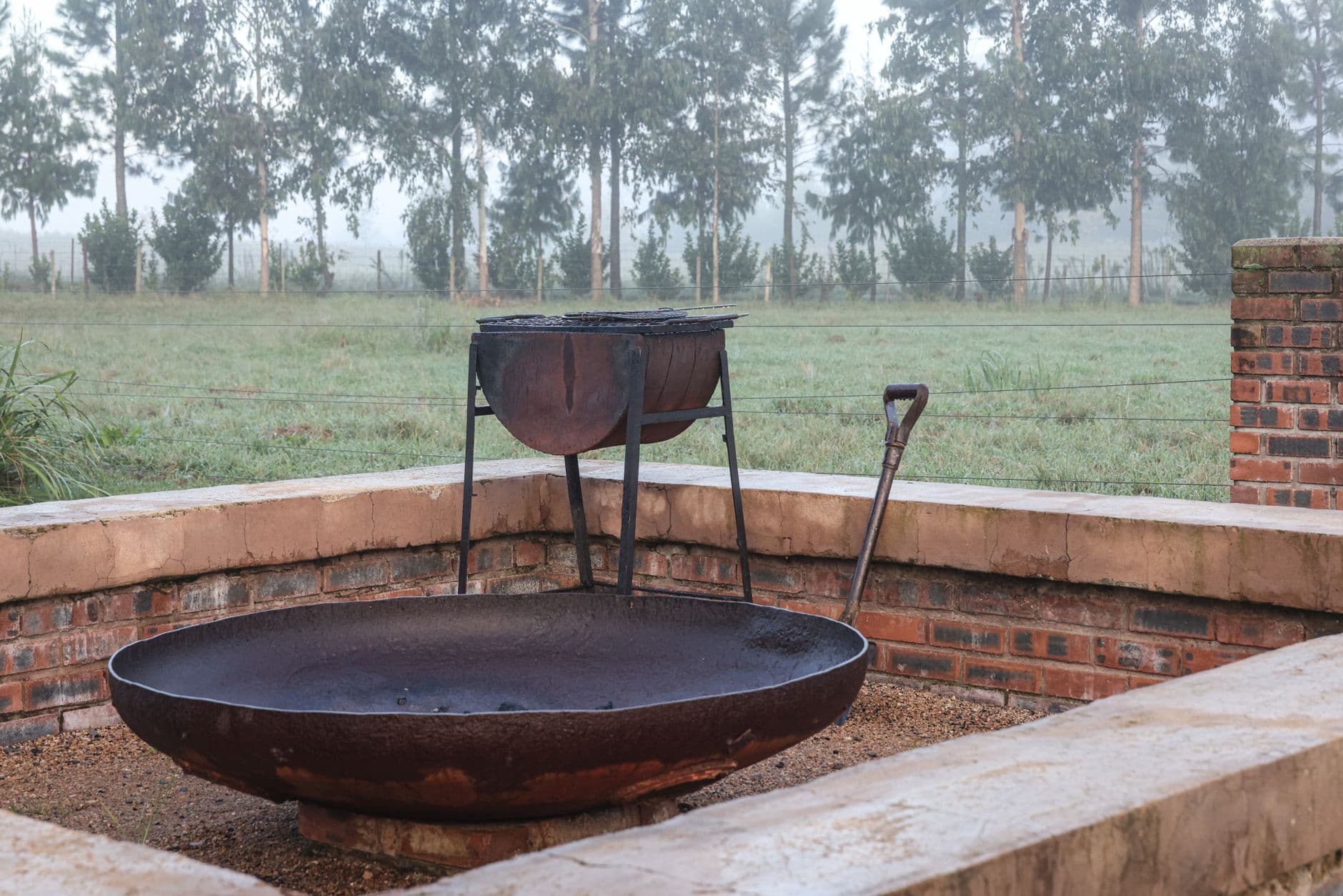 A foggy morning view of a rustic outdoor fireplace surrounded by brick in a serene backyard setting.