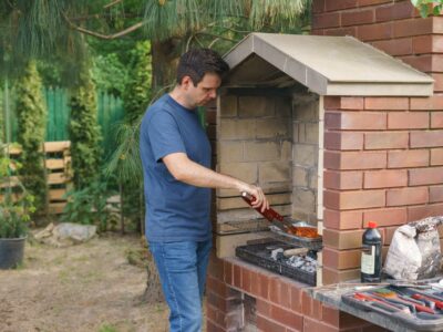 A man grills meat on a brick barbecue in the garden, showcasing outdoor cooking and leisure activity.